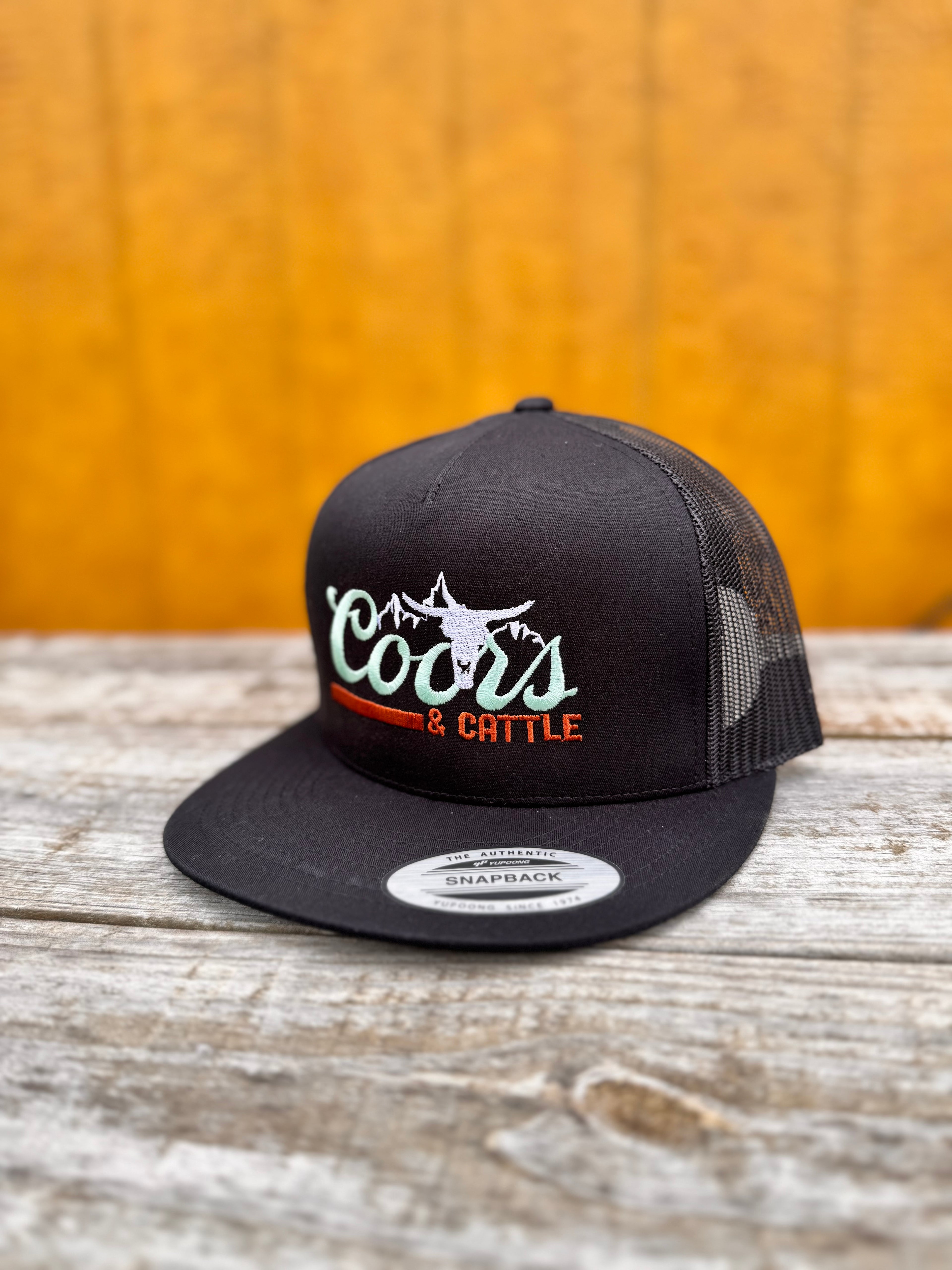 black trucker hat with 'Coors & Cattle' text on a wooden surface