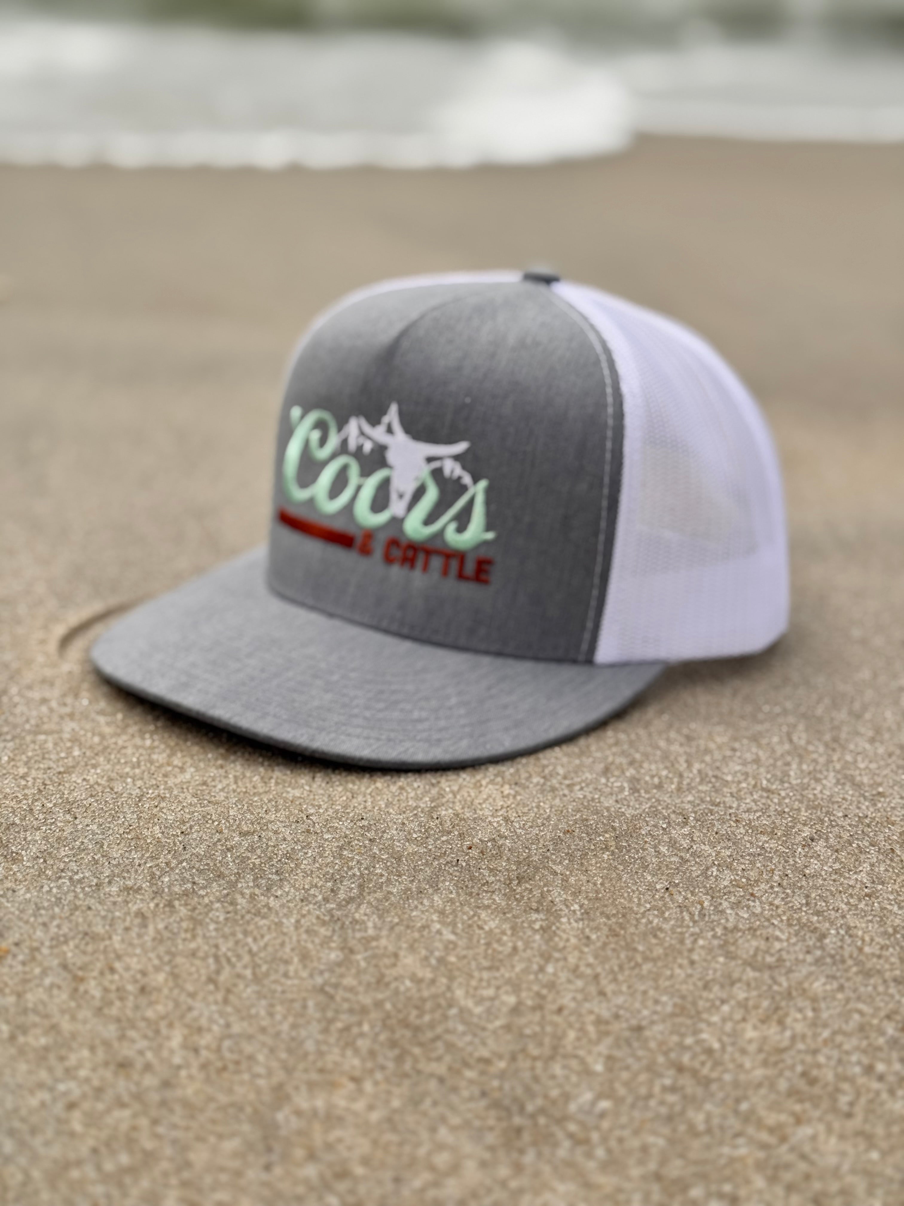 gray and white trucker hat with 'Coors & Cattle' text on a wooden surface