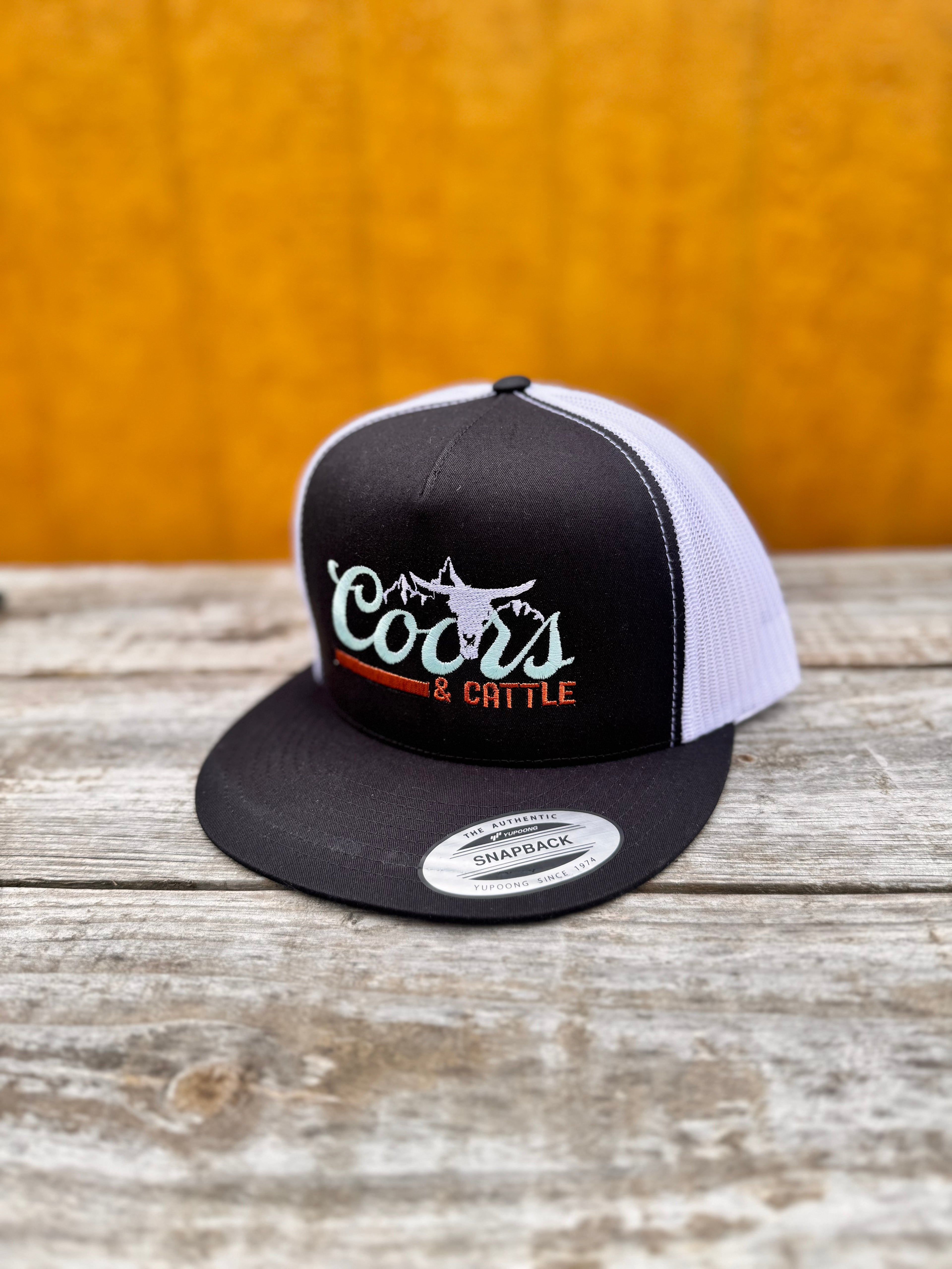 black and white trucker hat with 'Coors & Cattle' text on a wooden surface