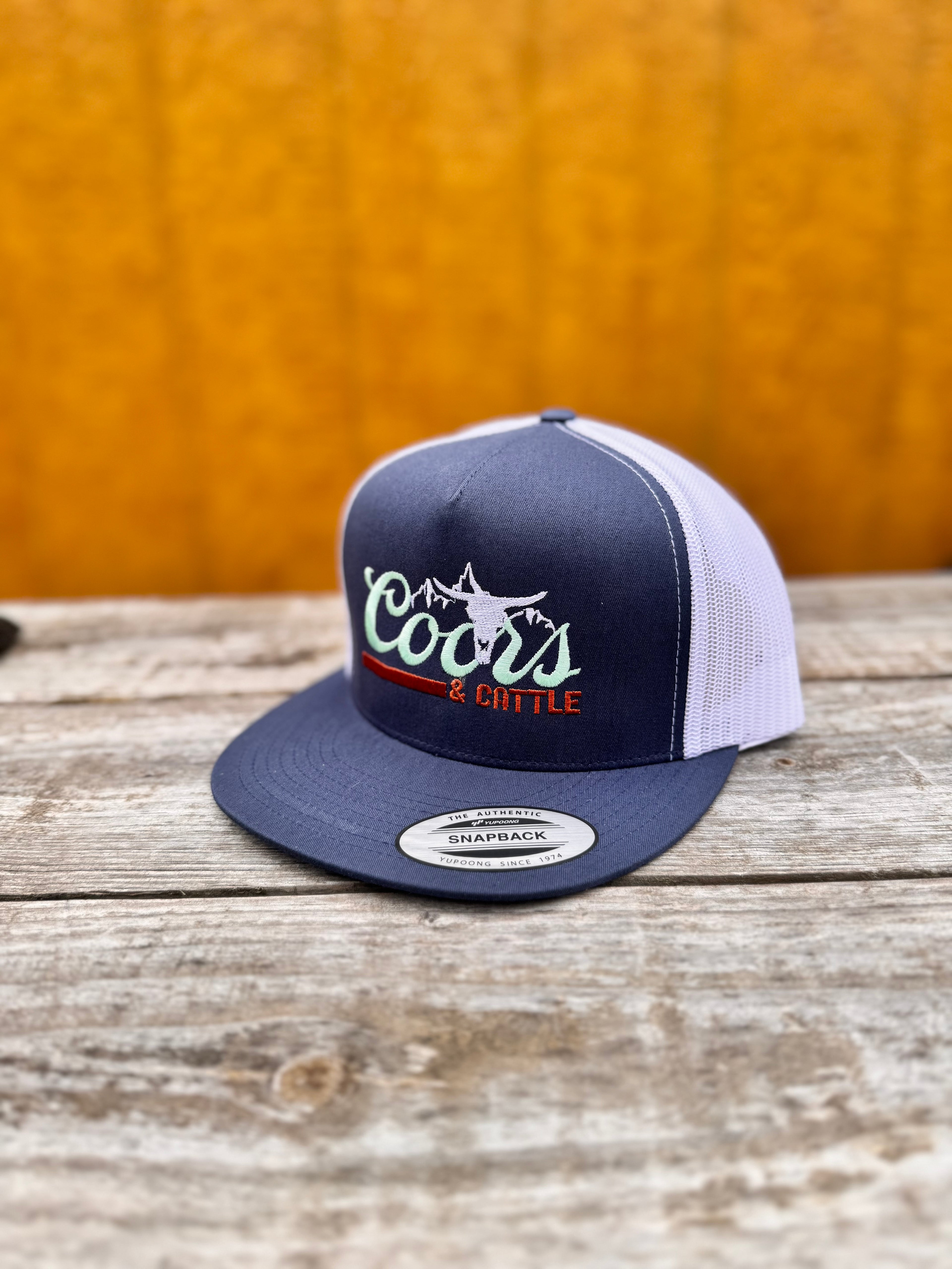 navy and white trucker hat with 'Coors & Cattle' text on a wooden surface