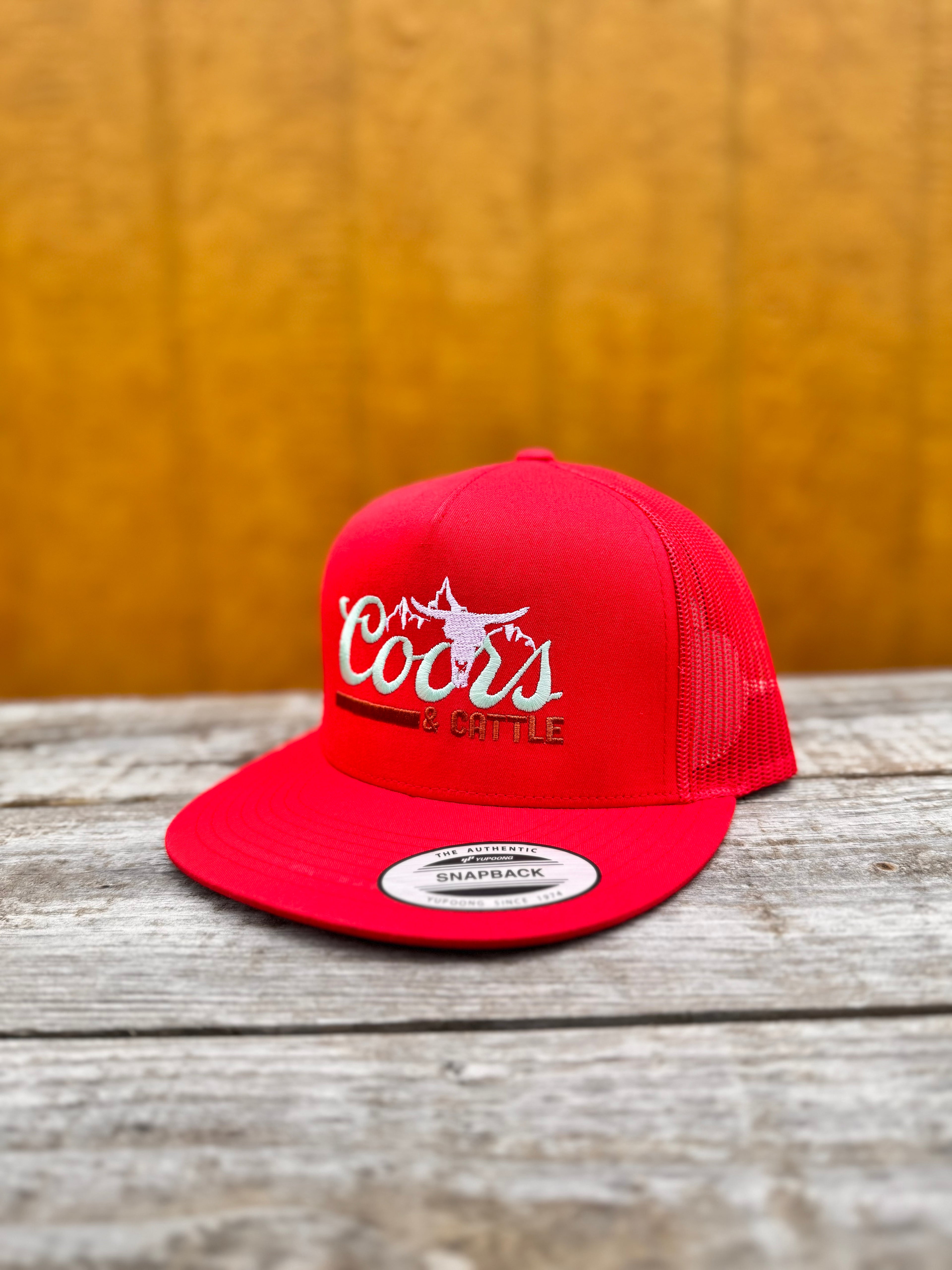 red trucker hat with 'Coors & Cattle' text on a wooden surface