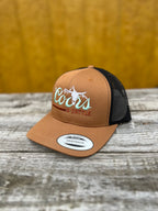 brown and black trucker hat with 'Coors & Cattle' text on a wooden surface