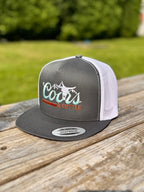 gray and white trucker hat with 'Coors & Cattle' text on a wooden surface