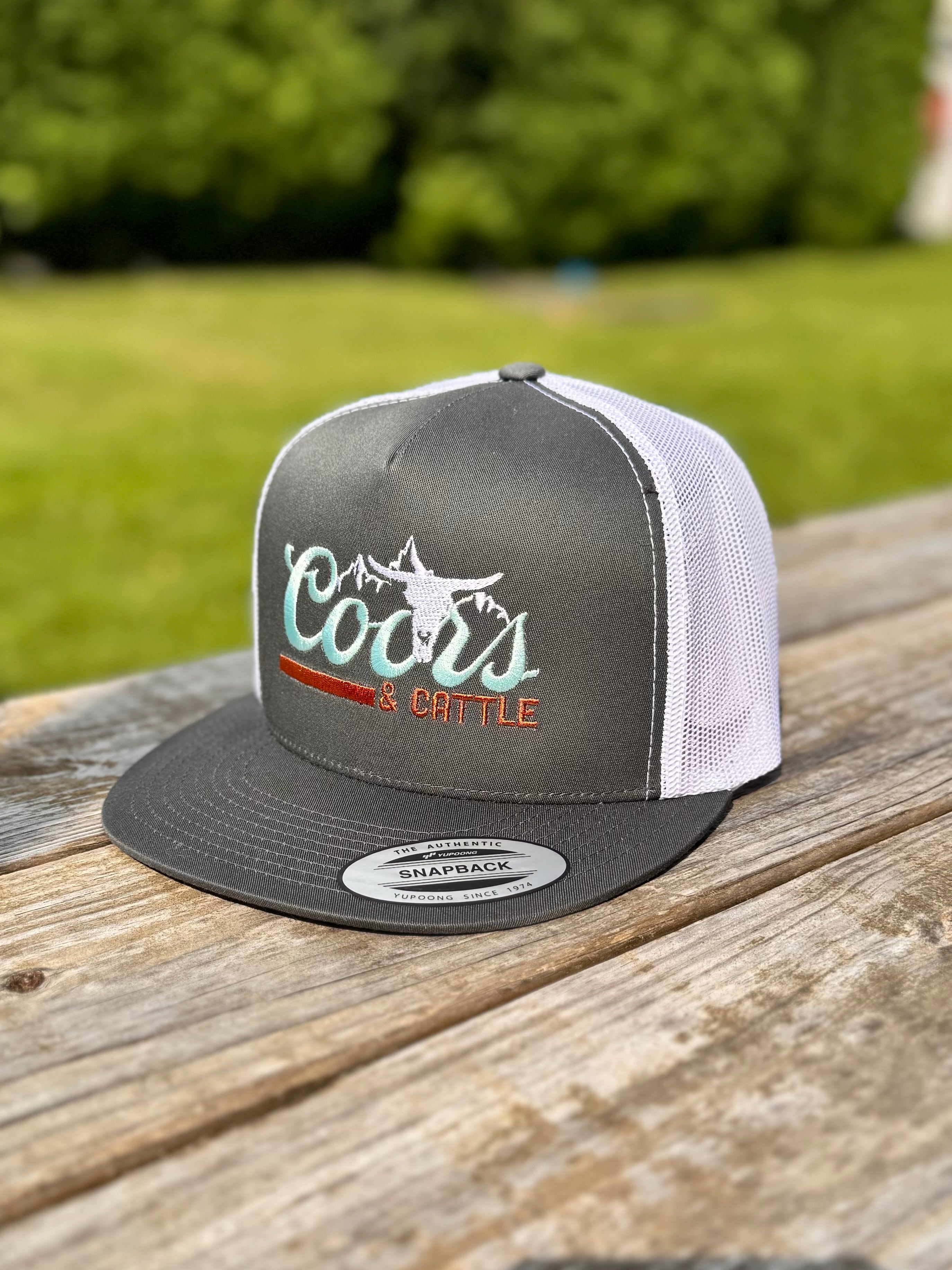 gray and white trucker hat with 'Coors & Cattle' text on a wooden surface