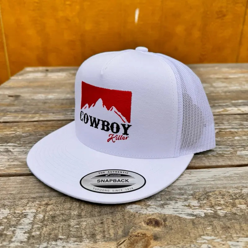 White trucker snapback hat with red and black 'cowboy killer' text and mountain logo on a wooden surface