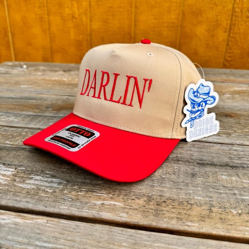 Tan and red snapback hat with 'Darlin' text on a wooden surface