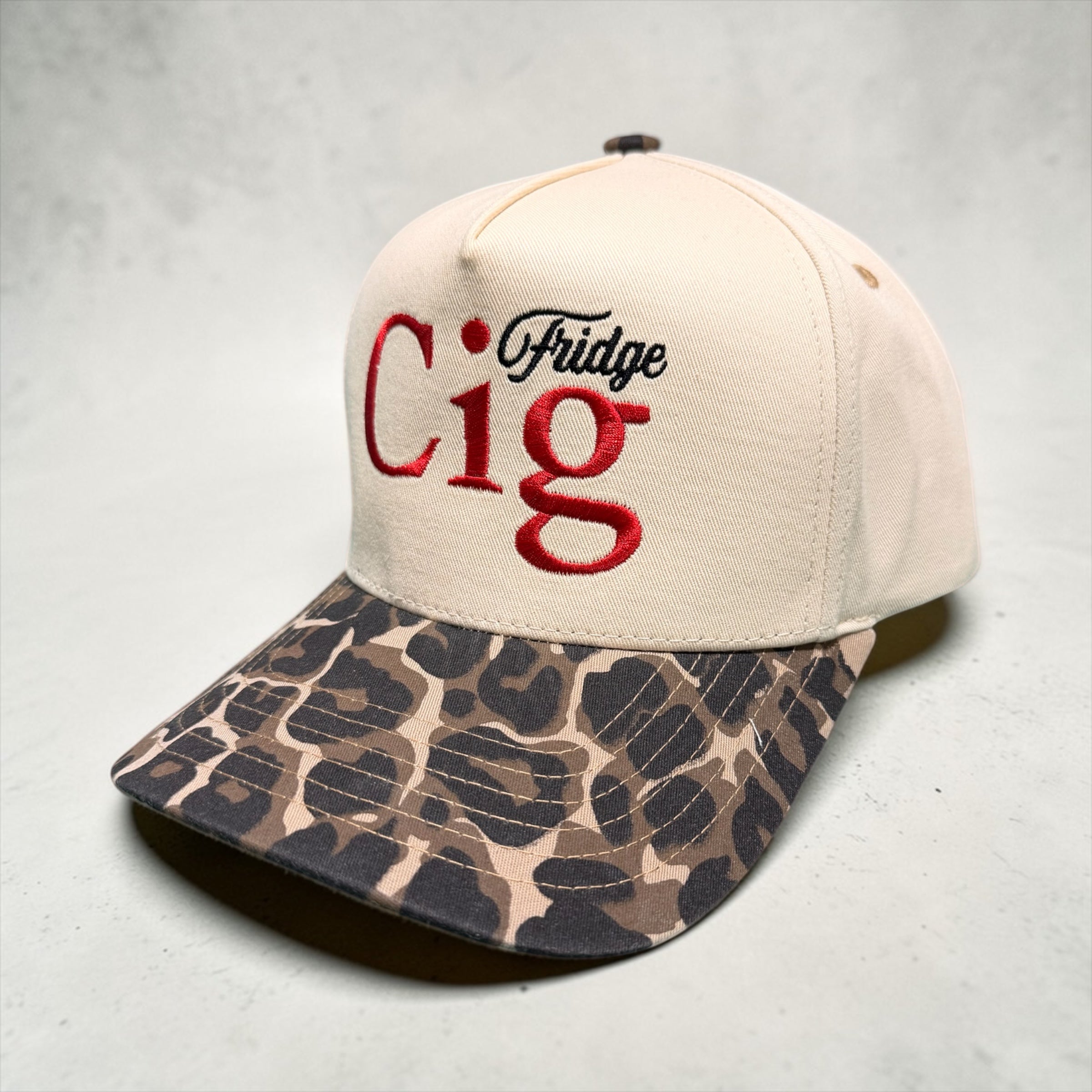 Beige snapback hat with "fridge cig" text and leopard camouflage brim on a gray background