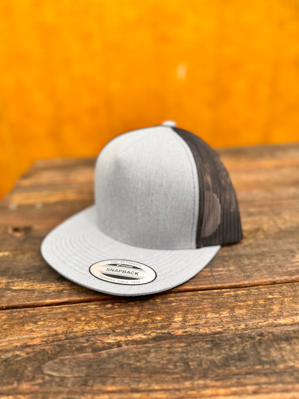 heather grey and black trucker hat on a wooden surface with a blurred orange background