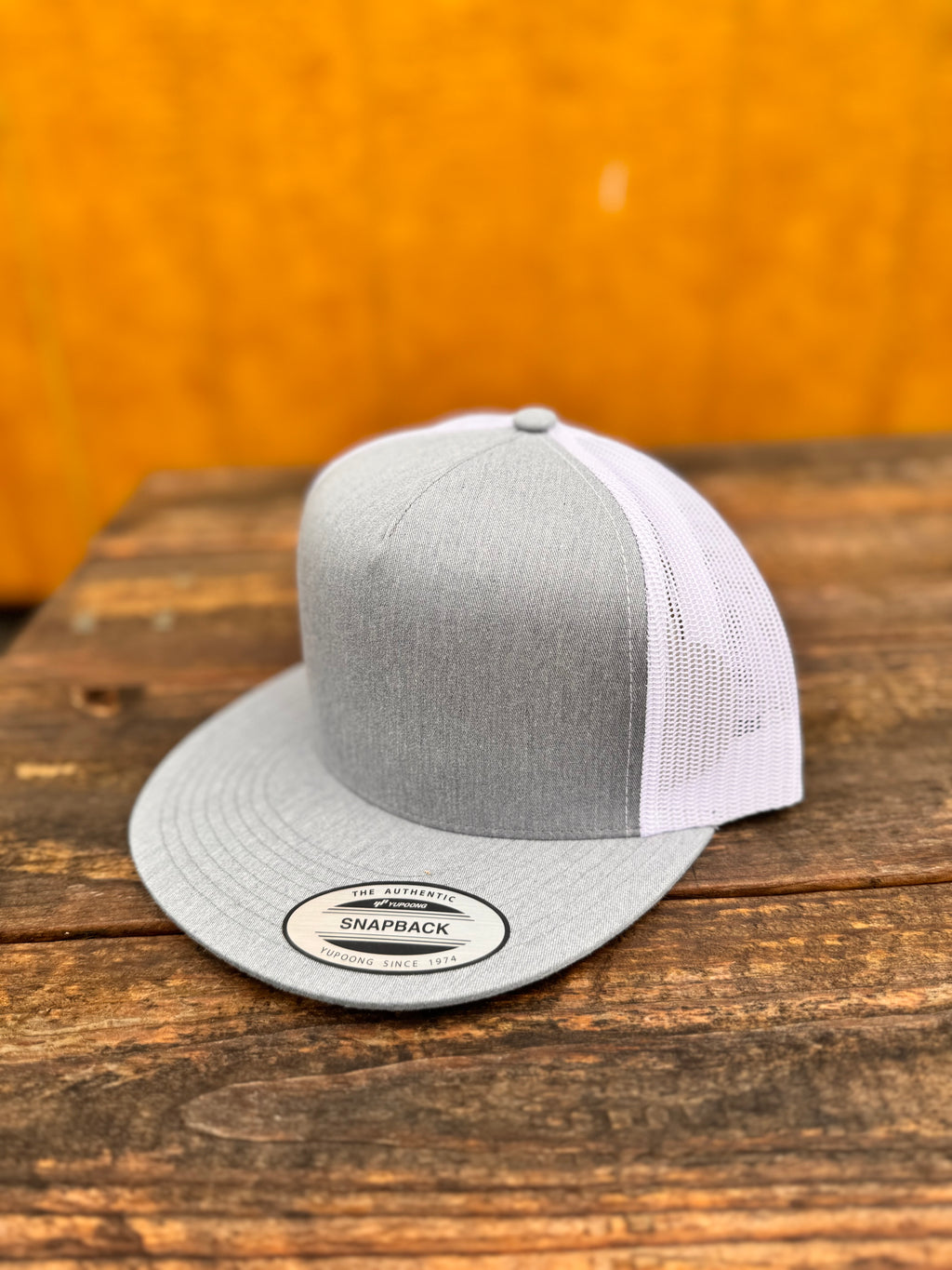 heather grey and white trucker cap on a wooden surface with a yellowish-brown background