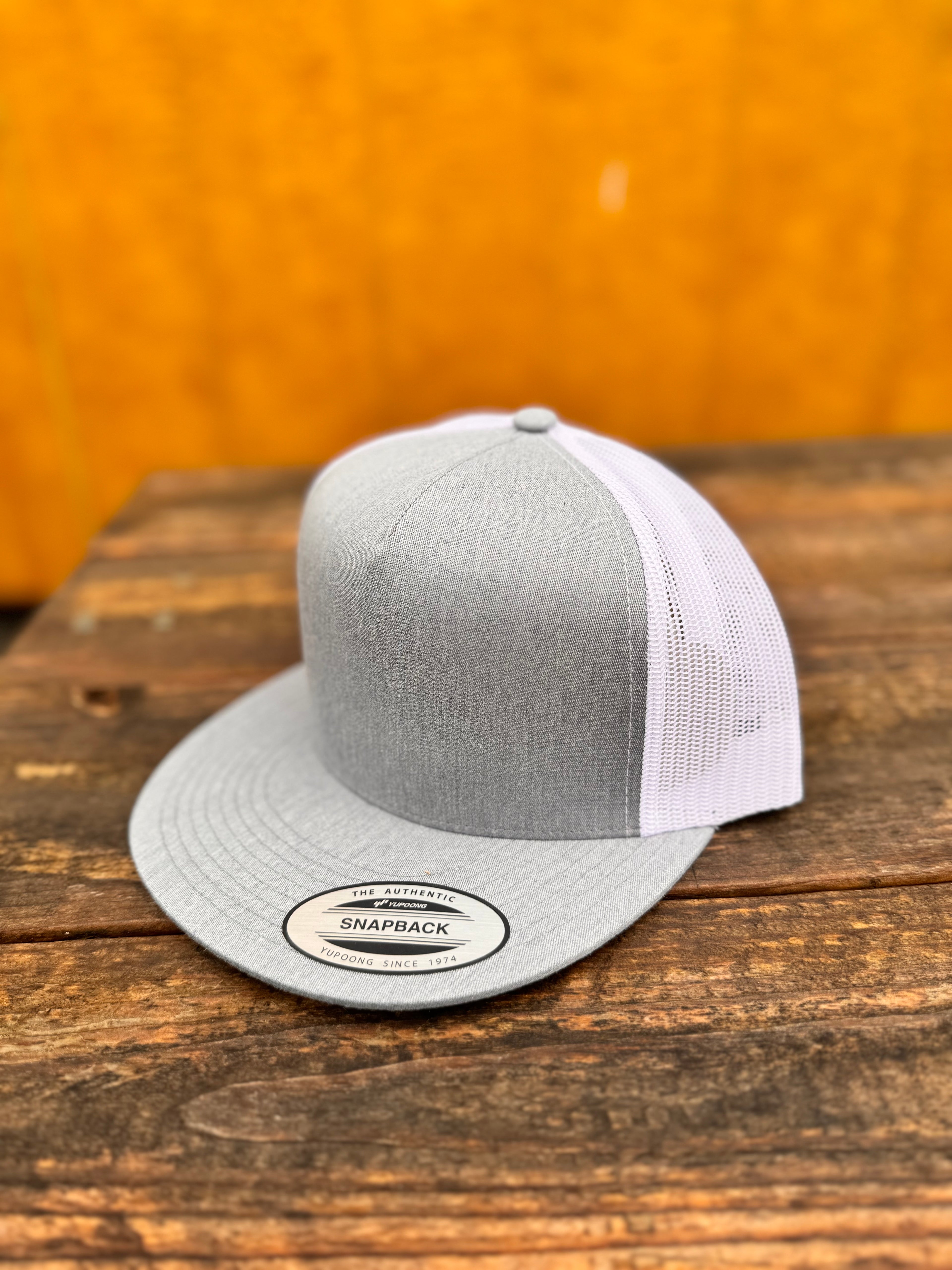 heather grey and white trucker cap on a wooden surface with a yellowish-brown background
