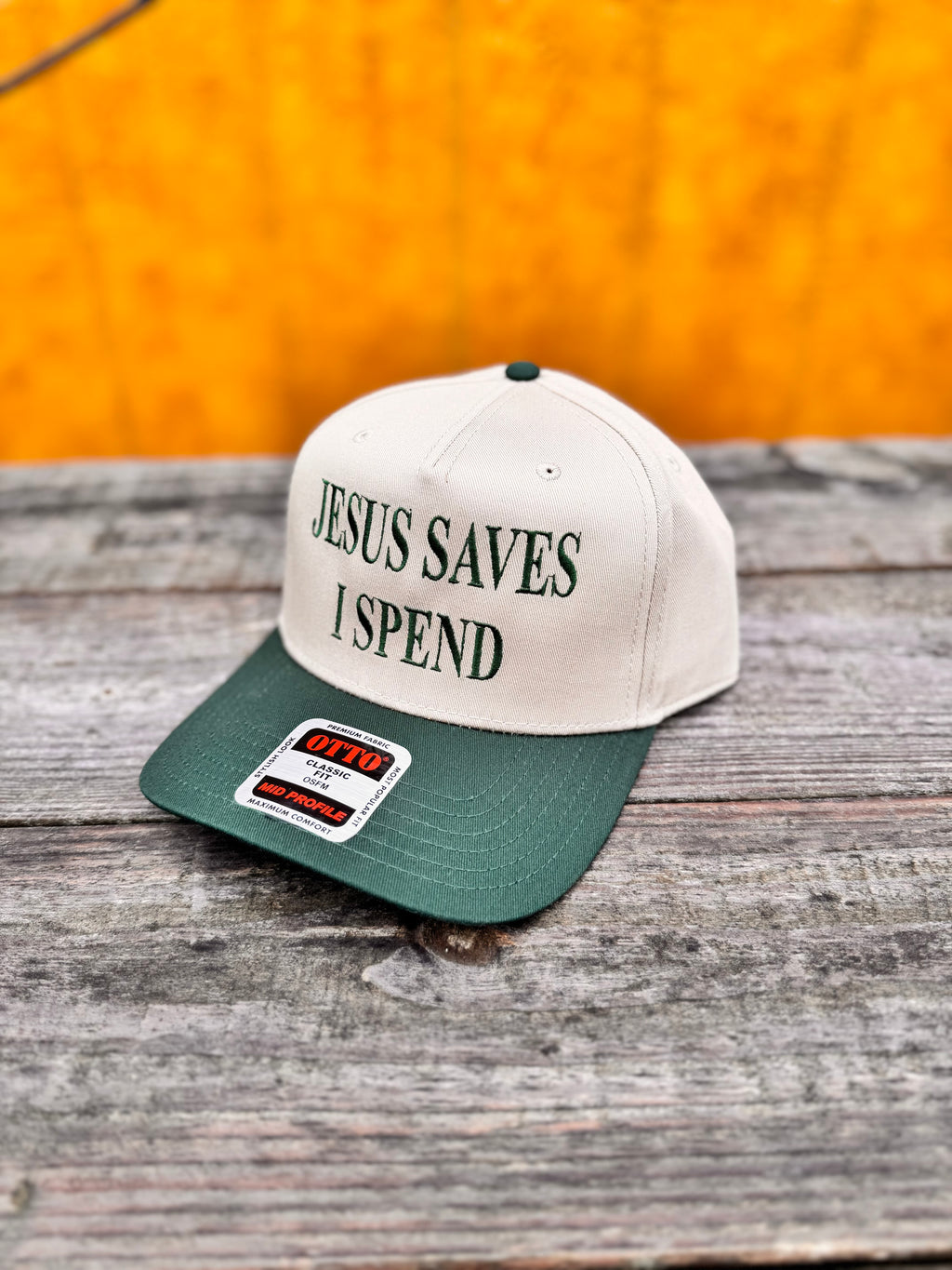 two tone beige and green snapchat hat with matching green  'Jesus Saves I Spend' text on a wooden surface