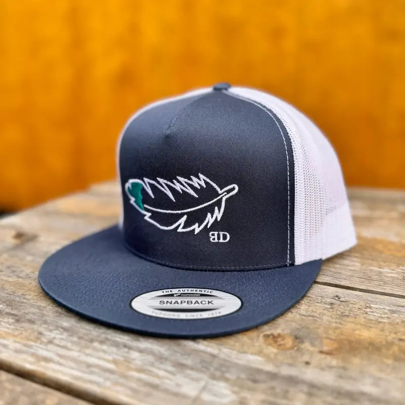 navy and white trucker cap with teal and white feather design on a wooden surface