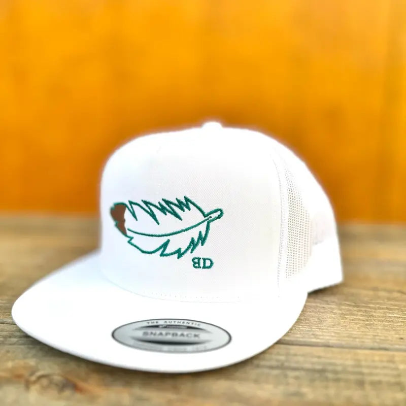 white trucker cap with green and brown feather design on a wooden surface