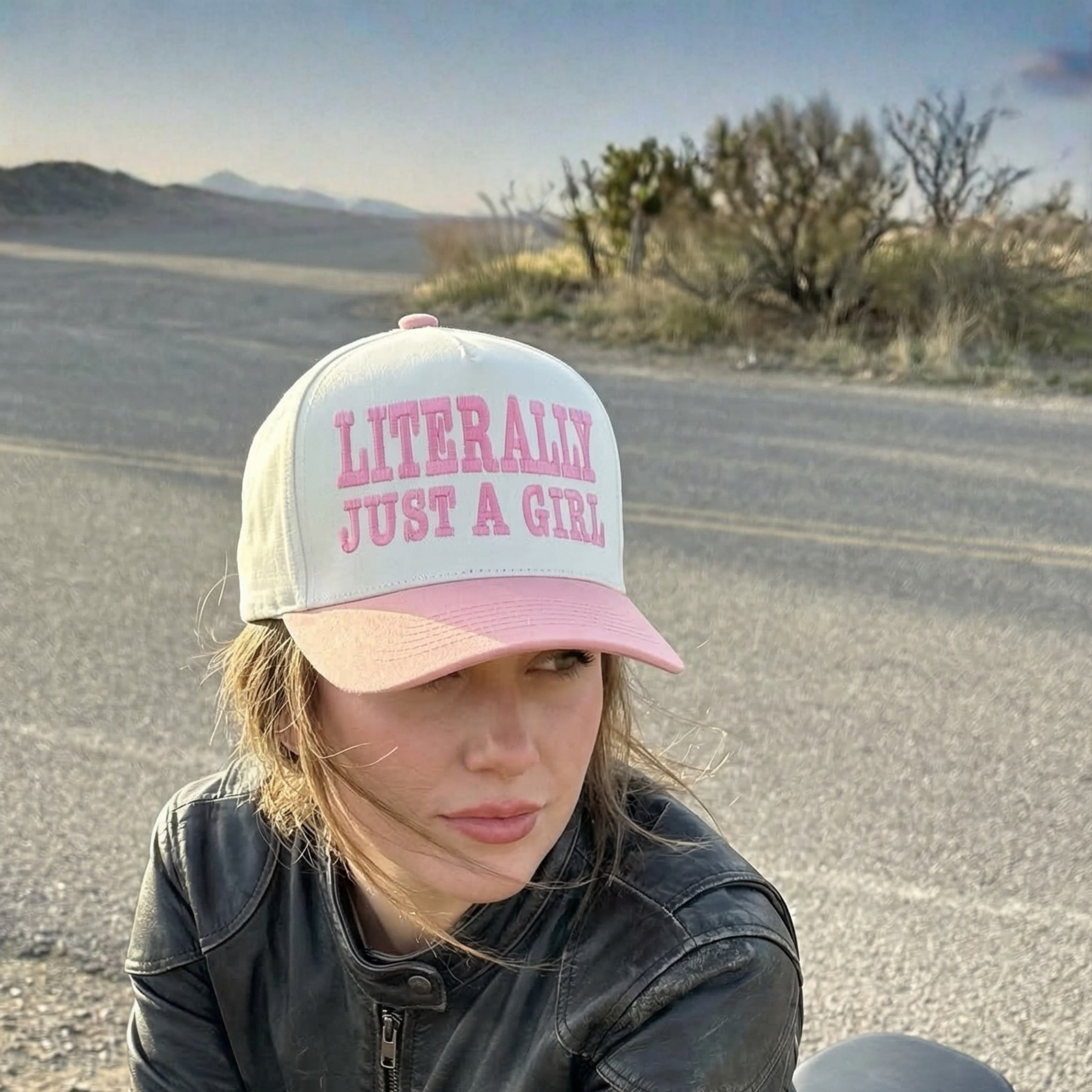 Person wearing a snapback hat with 'Literally Just a Girl' text in a desert road setting
