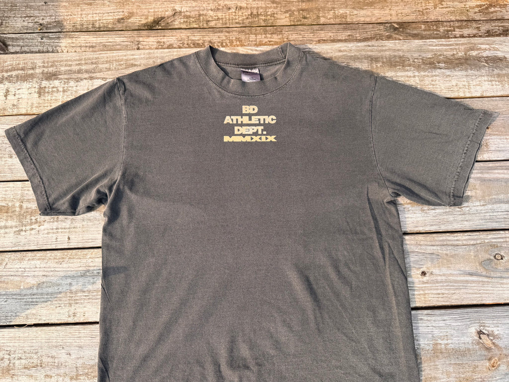 gray t-shirt with tan 'BD ATHLETIC DEPT.' text on a wooden table
