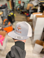 grey and white snapback hat with orange 'SAY WHEN' text held by a person in a store setting