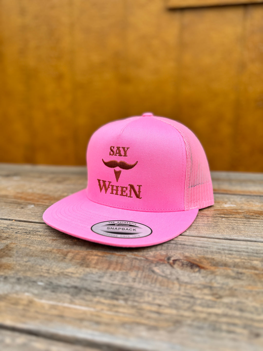 pink snapback hat with orange 'SAY WHEN' text on a wooden table