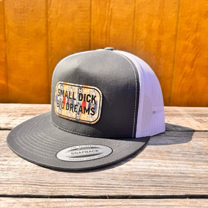 Charcoal and white hat with 'Small D*ck Big Dreams' patch on a wooden surface.
