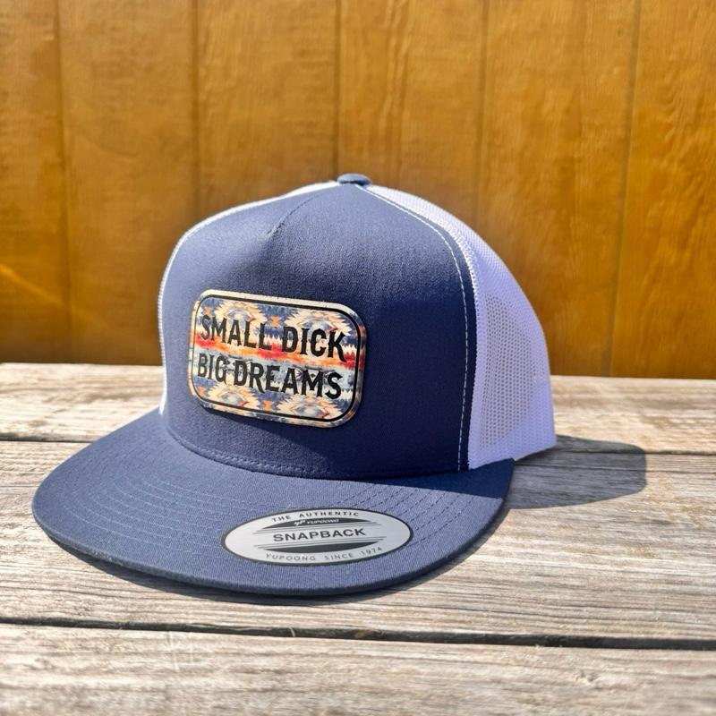 Navy blue and white snapback hat with 'Small D*ck Big Dreams' patch on a wooden surface.