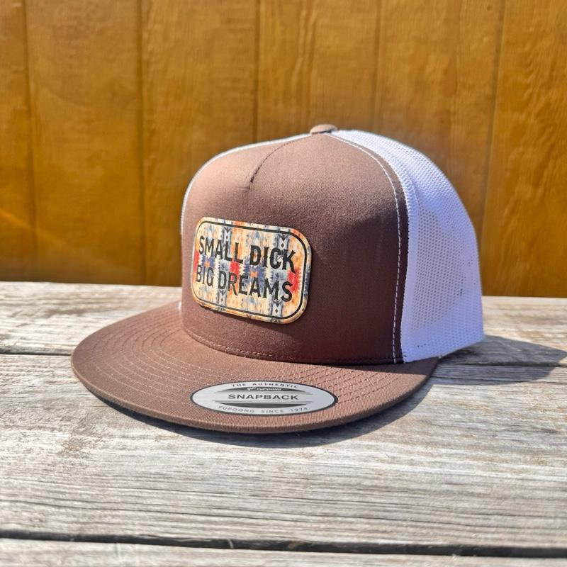 rootbeer and white snapback hat with 'Small D*ck Big Dreams' patch on a wooden surface.