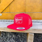 Red snapback hat with white 'tattooed low life' text on a wooden surface