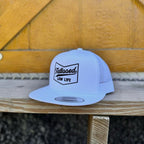 White snapback hat with black 'tattooed low life' text on a wooden surface