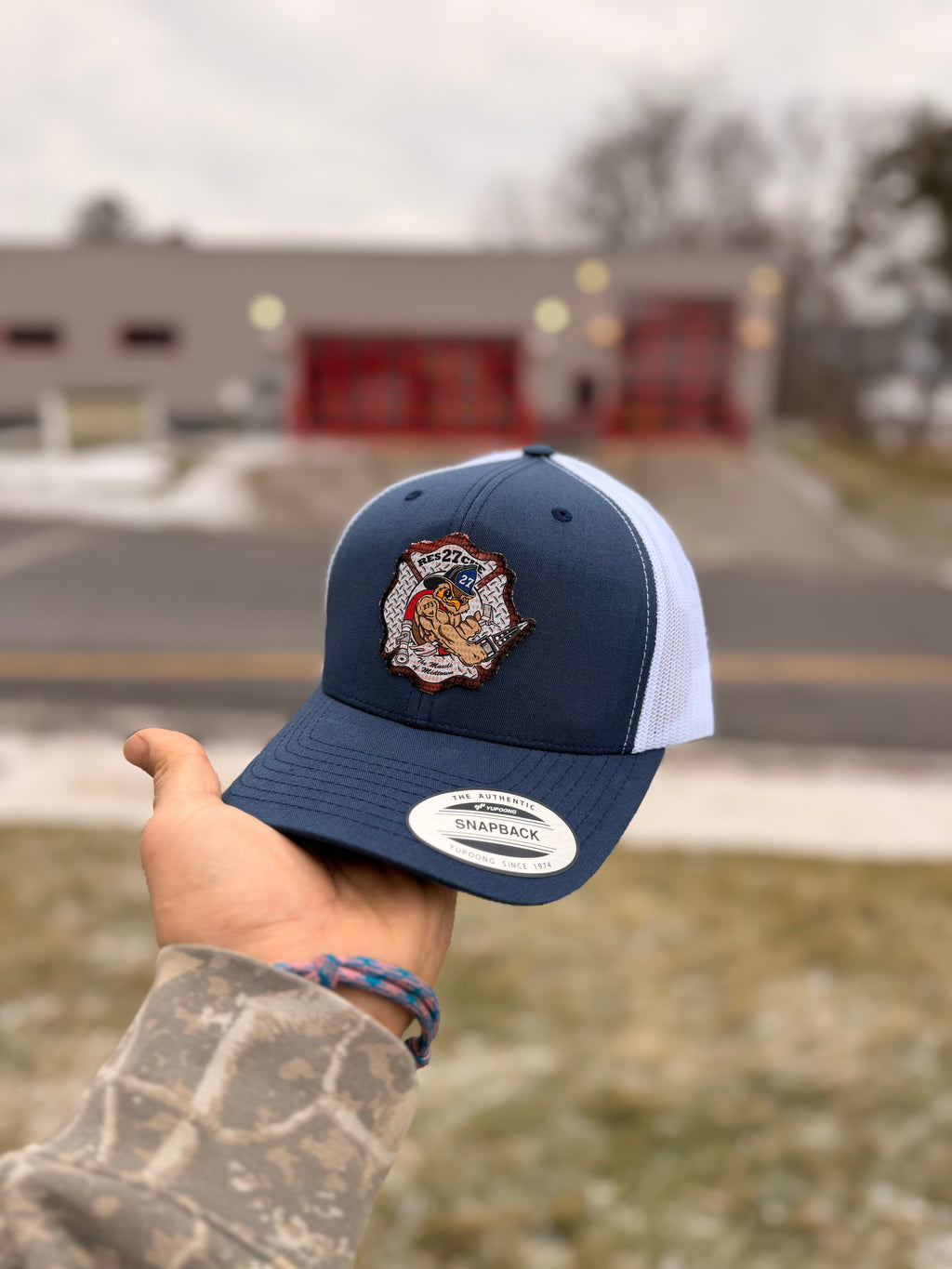 Navy and white cap with a logo held by a person outdoors.