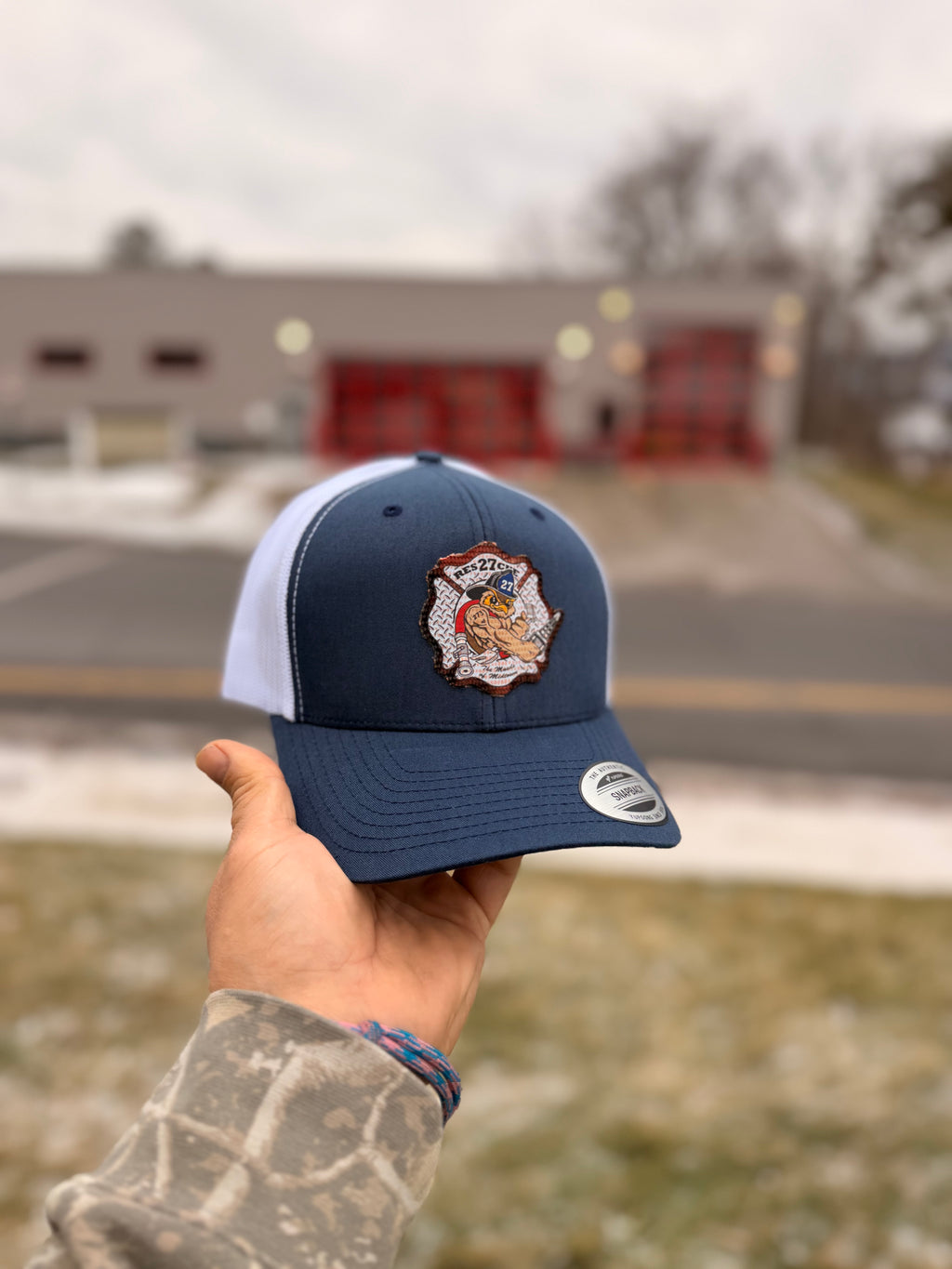 Navy blue cap with a logo held by a hand outdoors