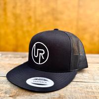 Black trucker snapback hat with a UR logo for "unhingedrancher" on a wooden surface