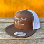 Rootbeer and white trucker snapback hat with 'Whiskey Bent & Hell Bound' text on a wooden surface with an orange background.