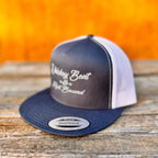 Navy and white snapback hat with 'whiskey bent and hell bound' text on a wooden surface and orange background