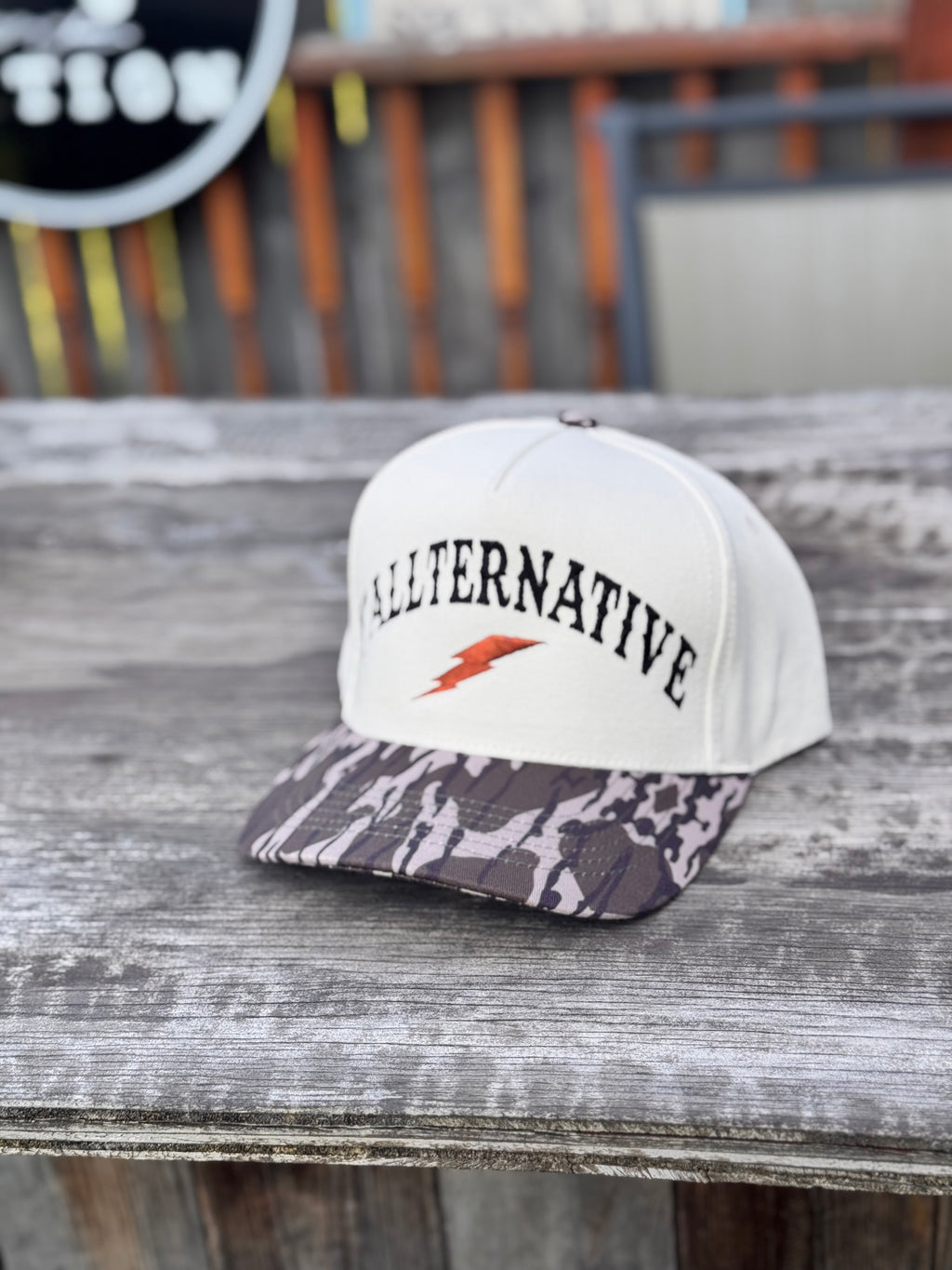 beige and camo snapback hat with black 'Y’ALLTERNATIVE' text on a wooden table