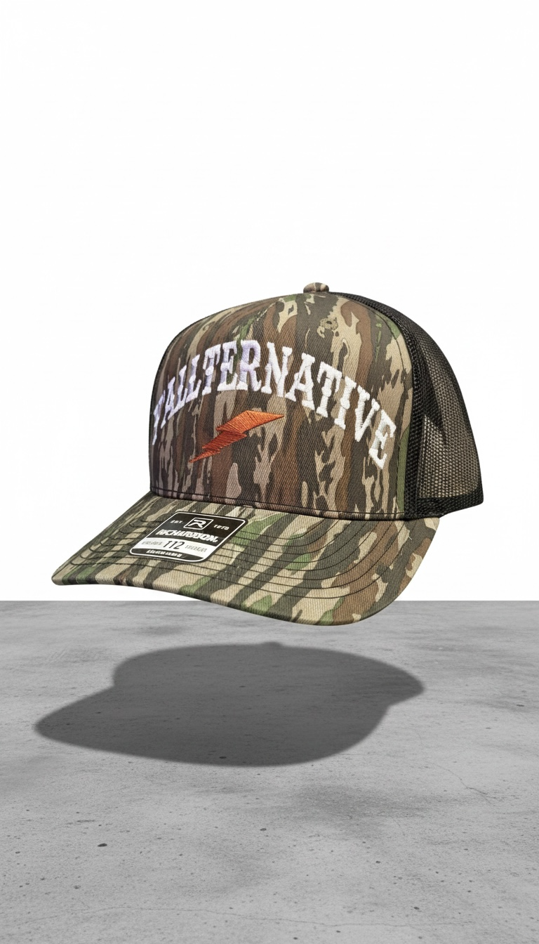 Camo and black snapback hat with 'YALLTERNATIVE' text and lightning bolt on a concrete and white background